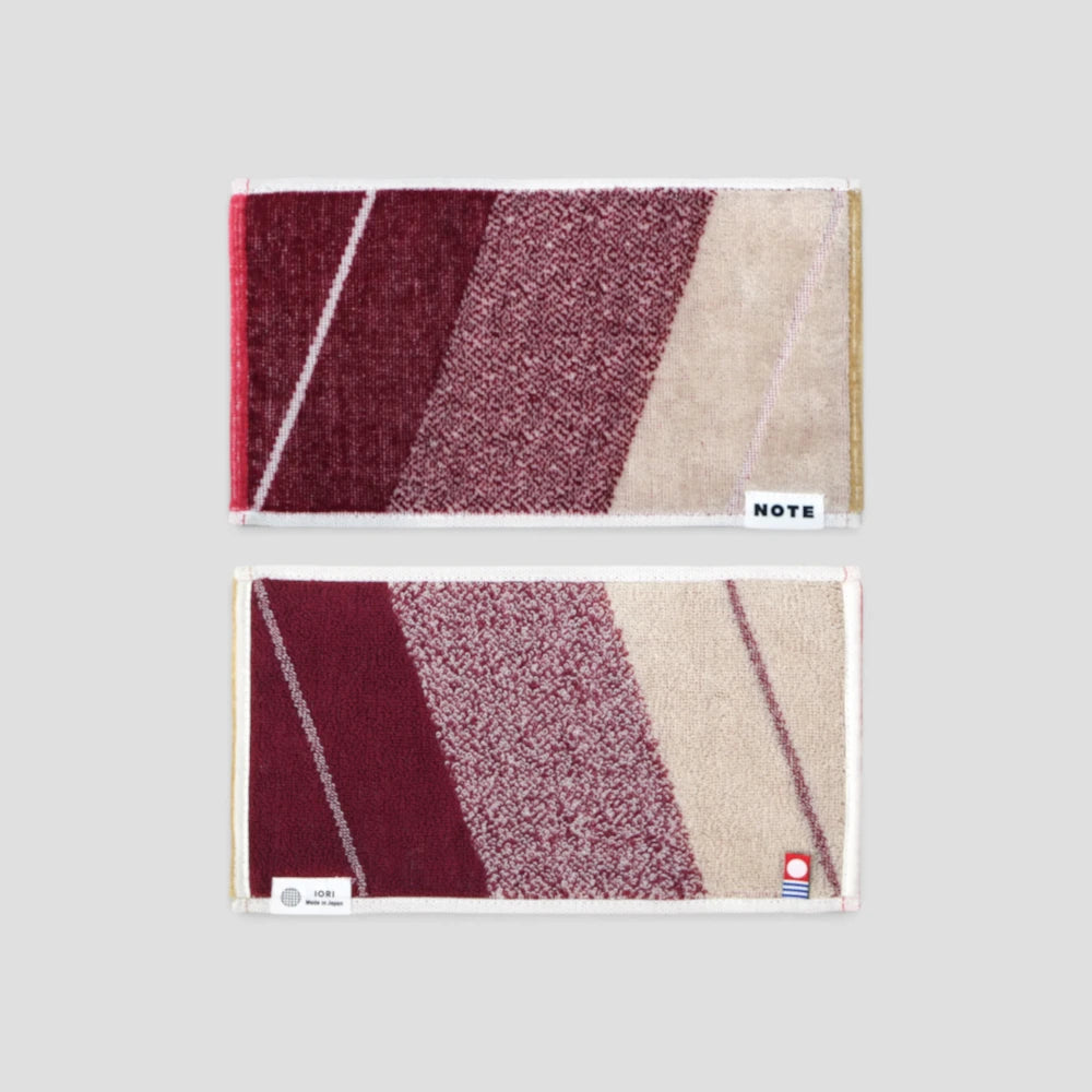 Two rectangular Imabari towel with a geometric diagonal stripe pattern in burgundy, mauve, and beige, displayed vertically on a light gray background. The top towel has a white label reading &