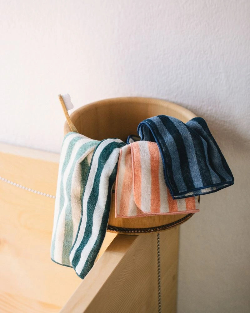 Striped Imabari towels hanging over a wooden bucket against a neutral wall.