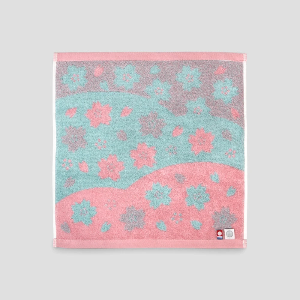 A square Imabari towel with a pink and teal floral pattern, displayed flat against a neutral light gray background.