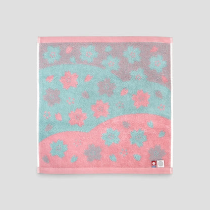 A square Imabari towel with a pink and teal floral pattern, displayed flat against a neutral light gray background.