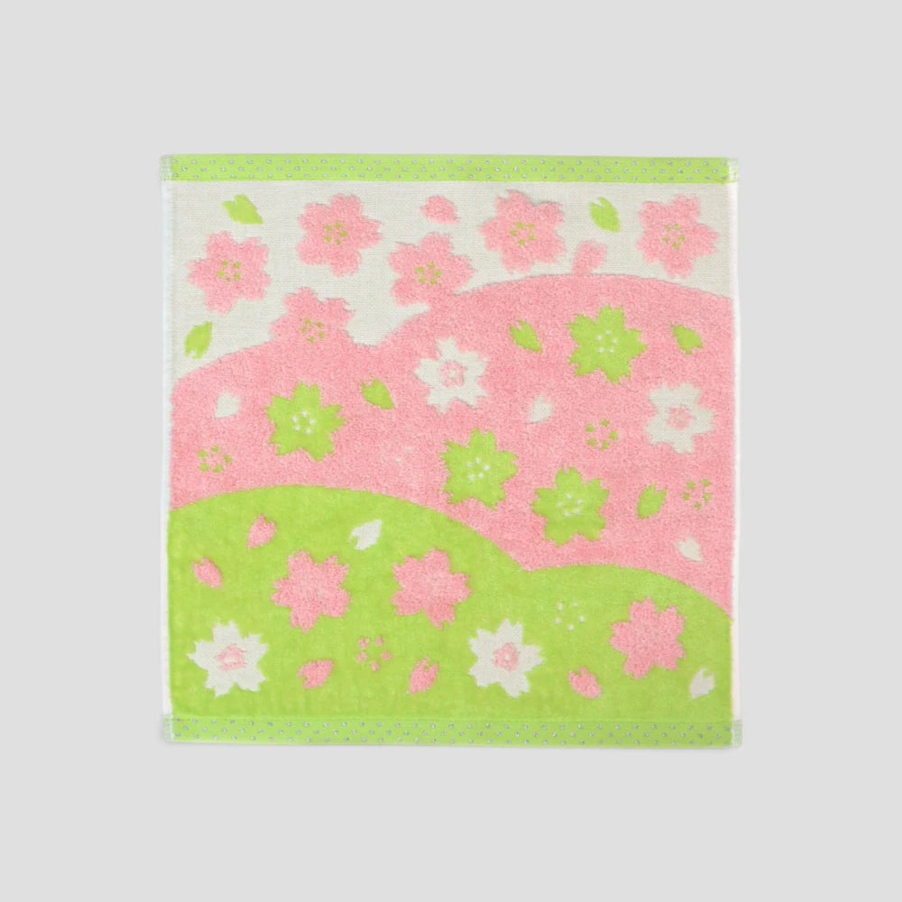 A square cotton Imabari wash towel with a pink and green cherry blossom pattern, displayed flat against a neutral light gray background.