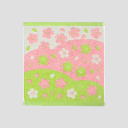 A square cotton Imabari wash towel with a pink and green cherry blossom pattern, displayed flat against a neutral light gray background.