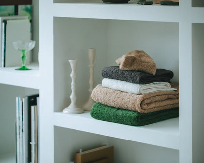 Stack of folded Imabari towels on a white shelf with decorative items.