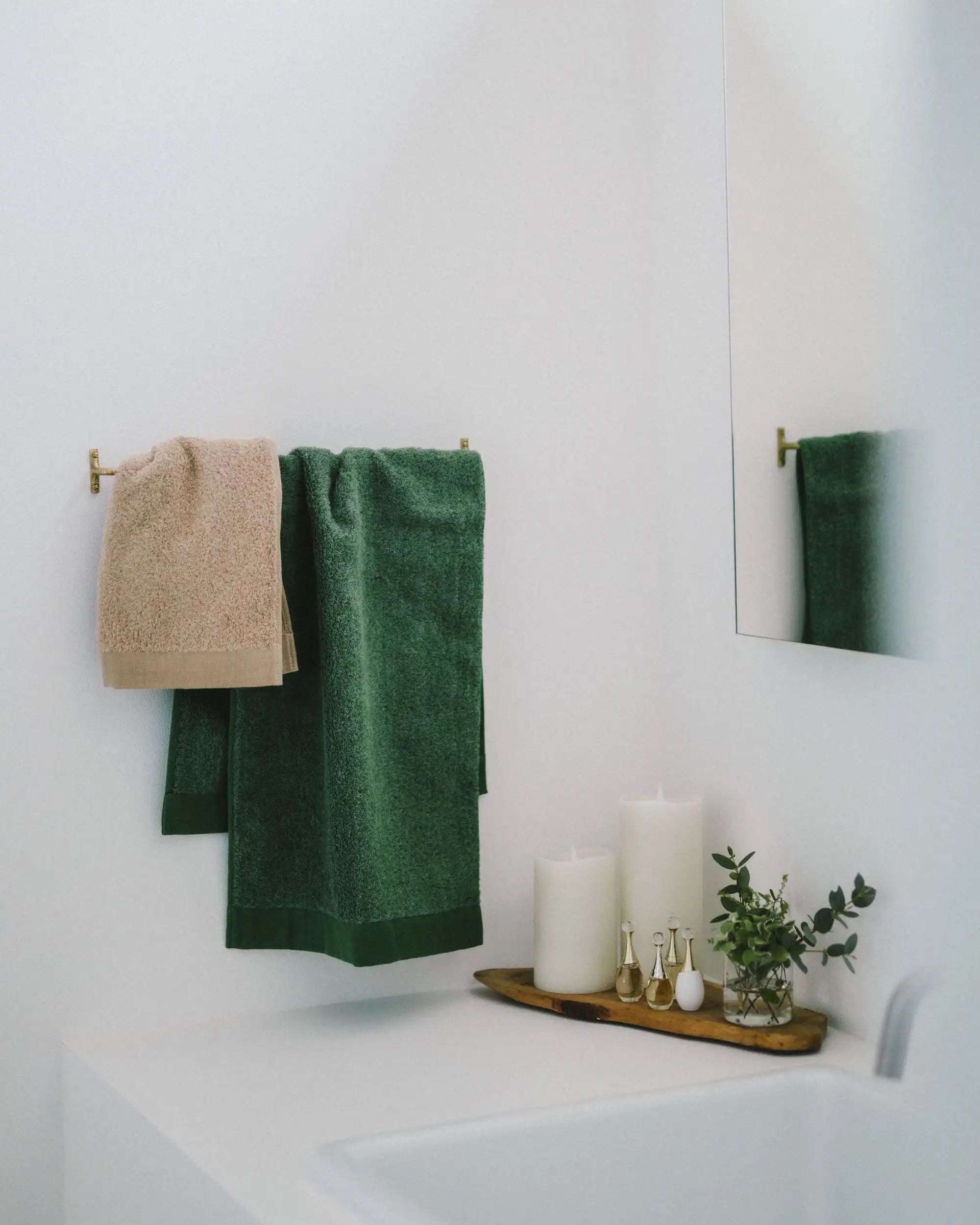 Green and beige Imabari towels hanging on a rack in a bathroom with candles and a plant.
