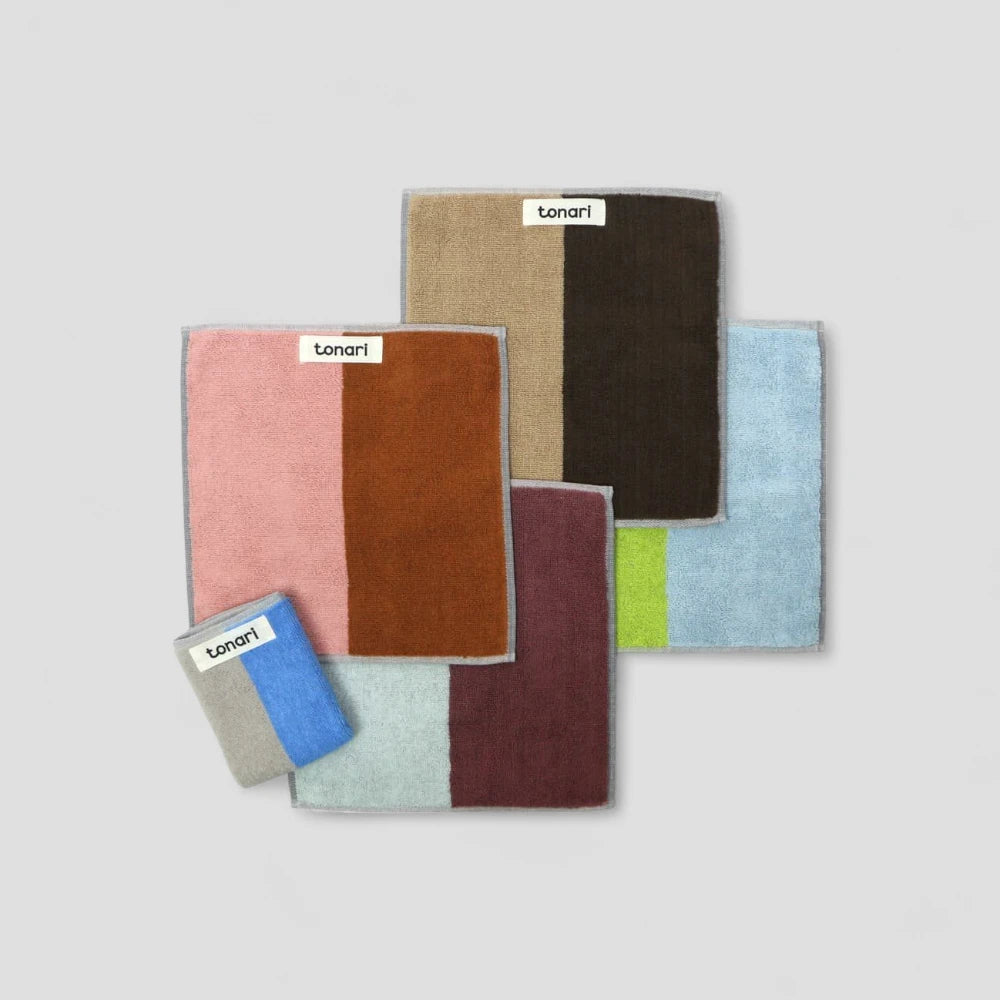 A collection of folded Imabari towle in various colors, including beige, brown, gray, pink, purple, blue, and green, displayed on a white background with the brand name &