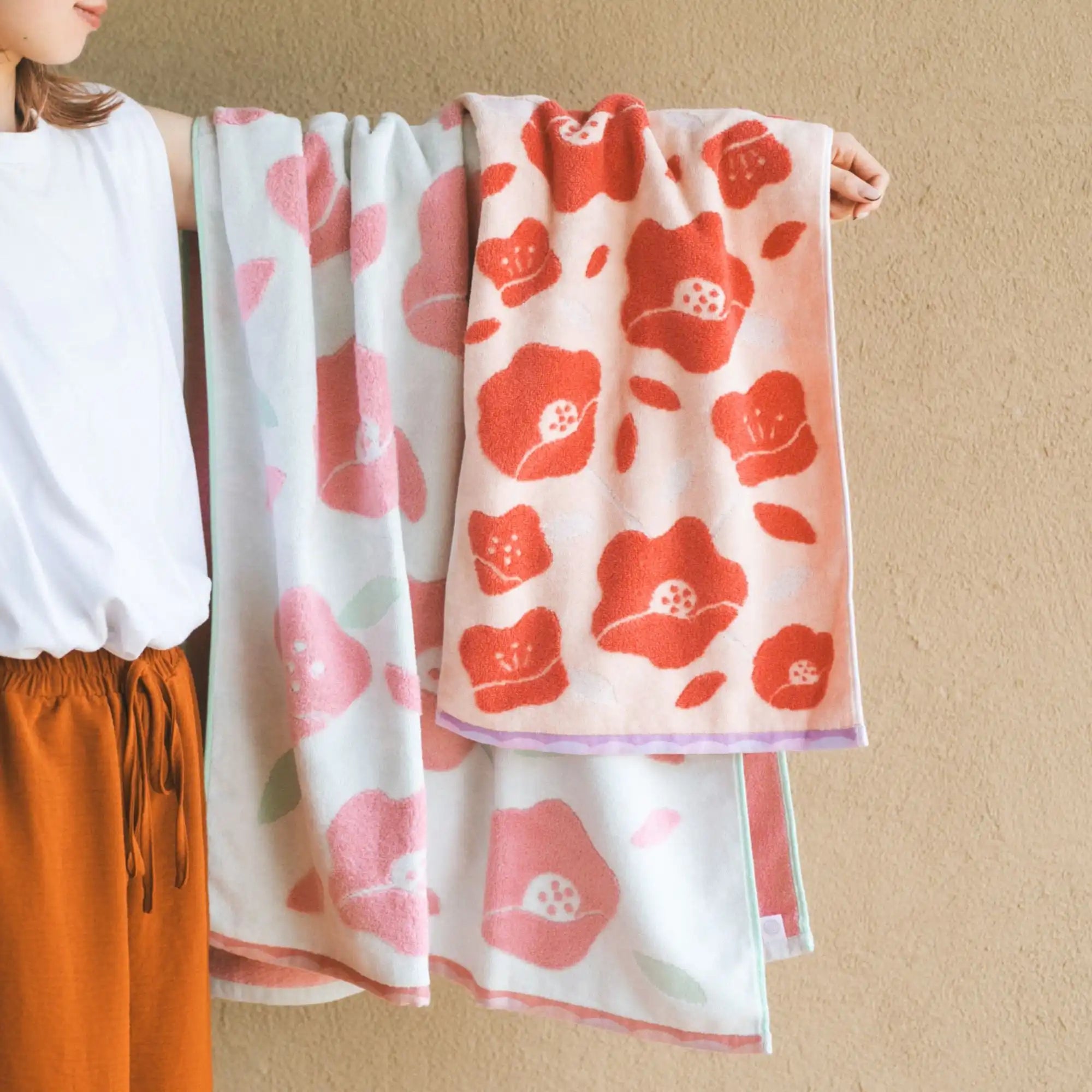 Person holding two floral Imabari towels with red and pink flowers on a beige background