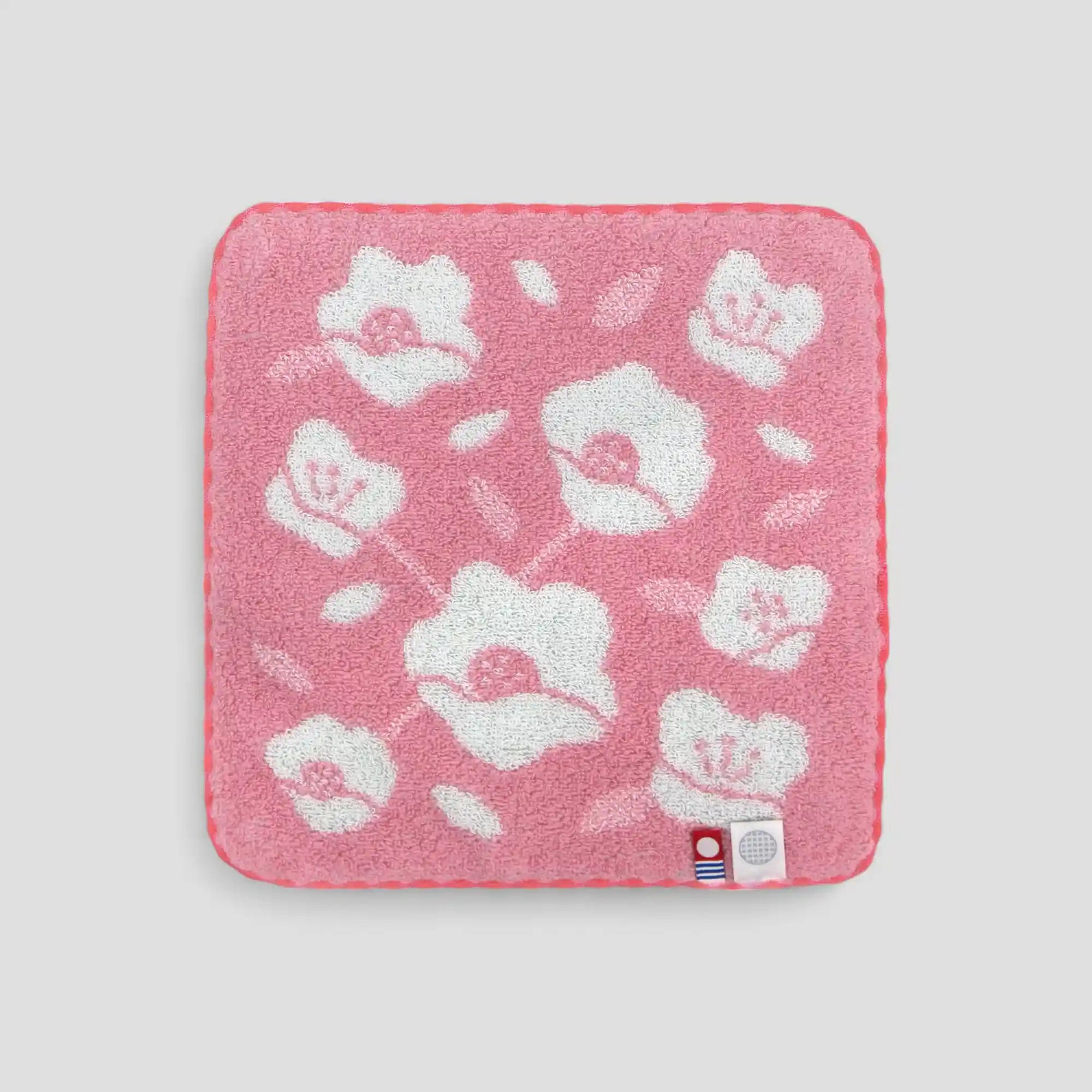 Pink Imabari towel with white floral pattern and labels of Iambari towel brand mark and IORI&