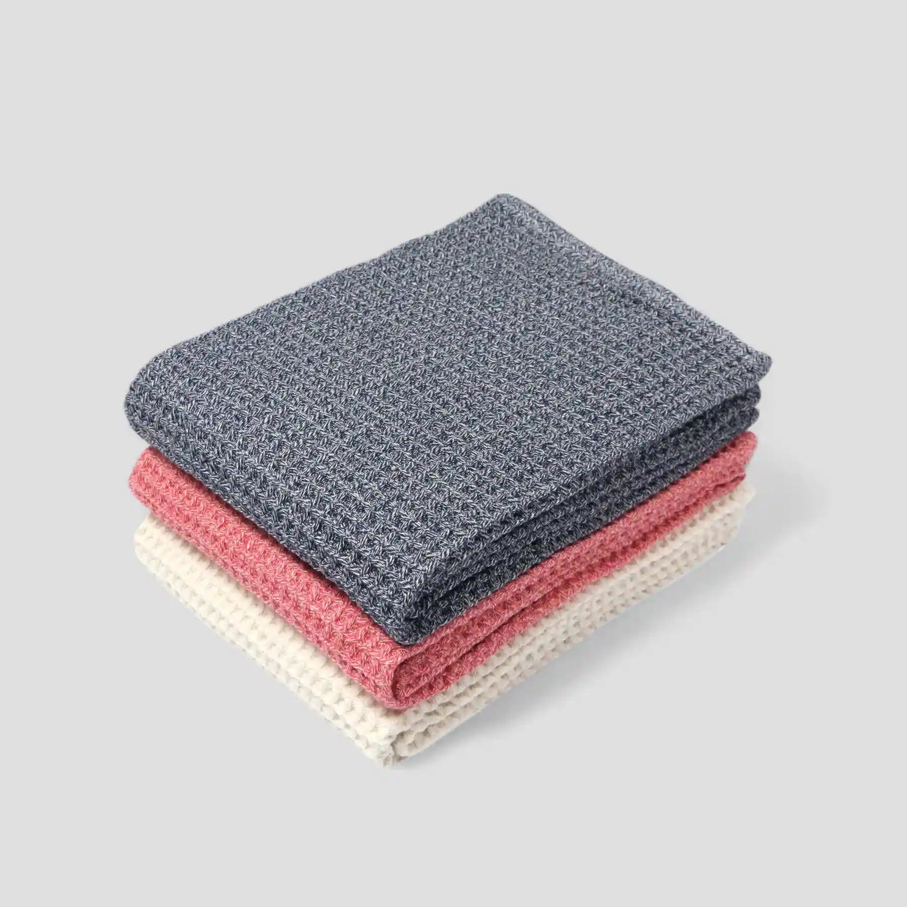 Stack of three folded Imabari towels in gray, pink, and beige on a light gray background