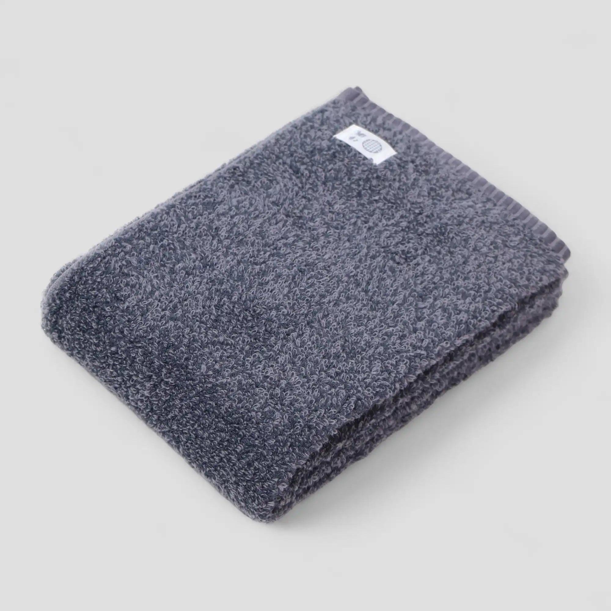Folded dark gray Imabari towel with a brand label on a light gray background