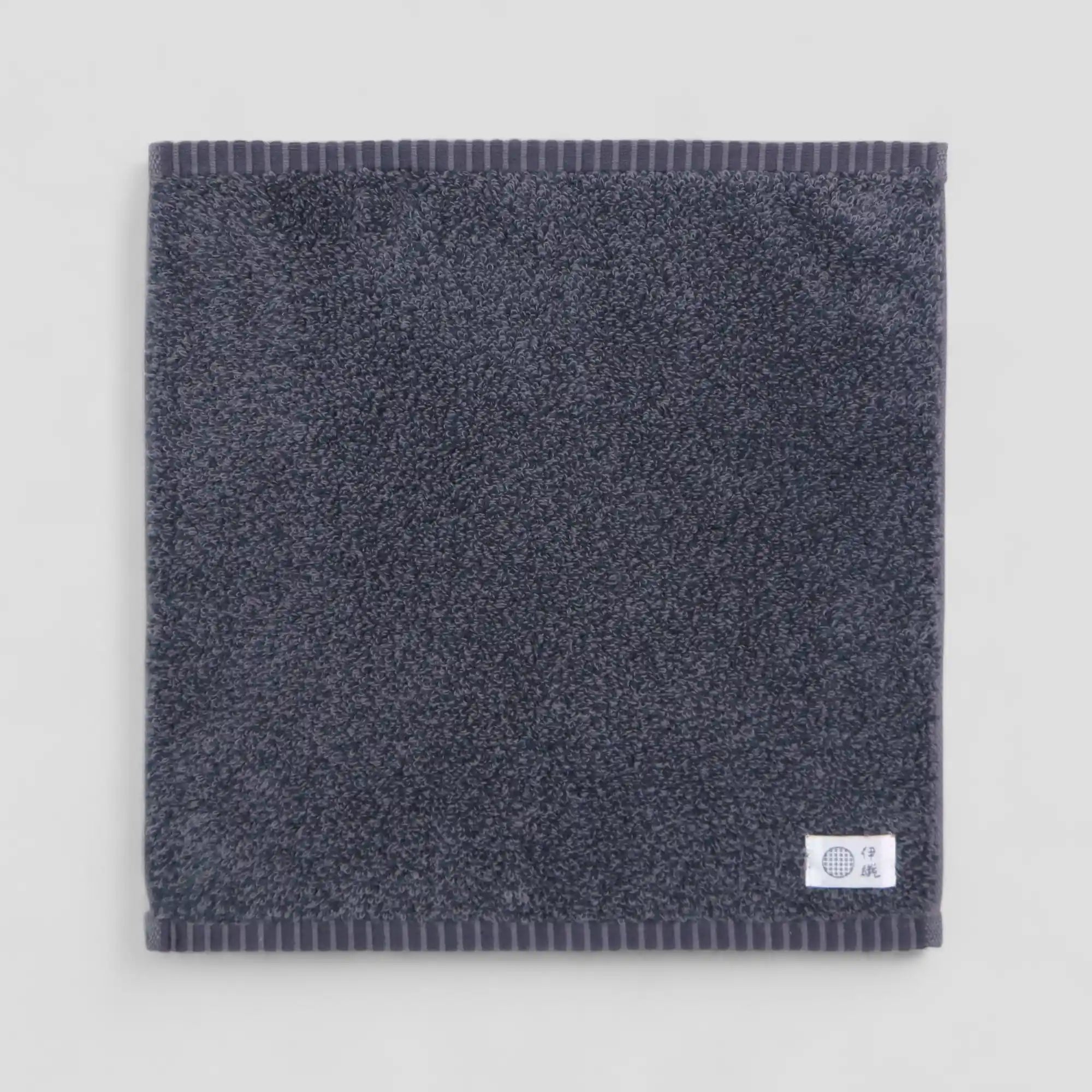 Dark gray Imabari towel with a brand label on a light gray background