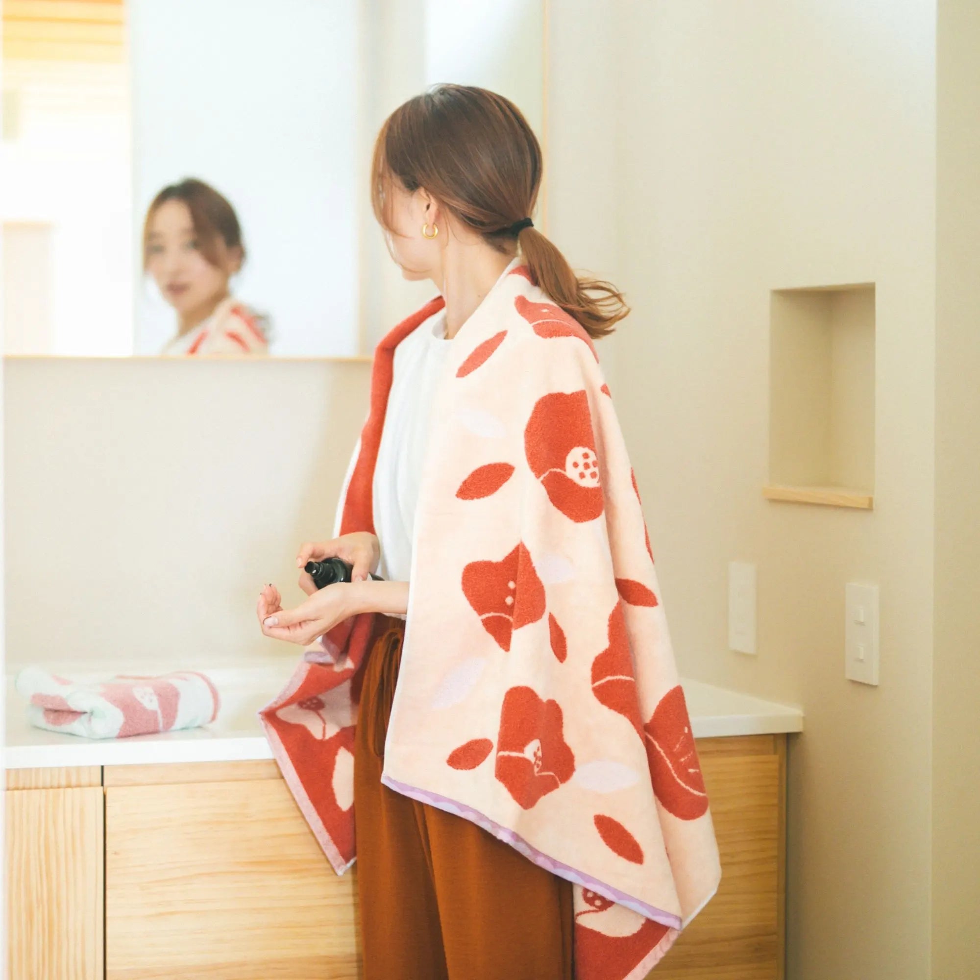 Woman in a bathroom wearing a red floral Imabari towel over her shoulders.