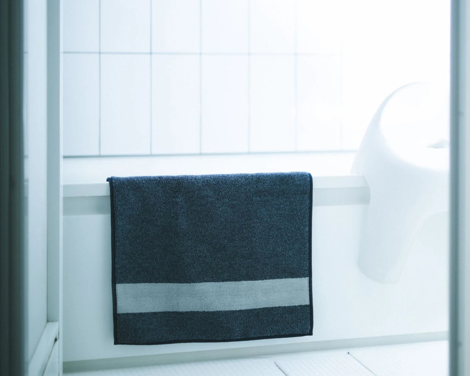 Navy Imabari towel bath mat on a white bathtub with tiled wall