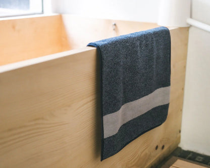 Navy Imabari towel bath mat hanging on a wooden bathtub corner
