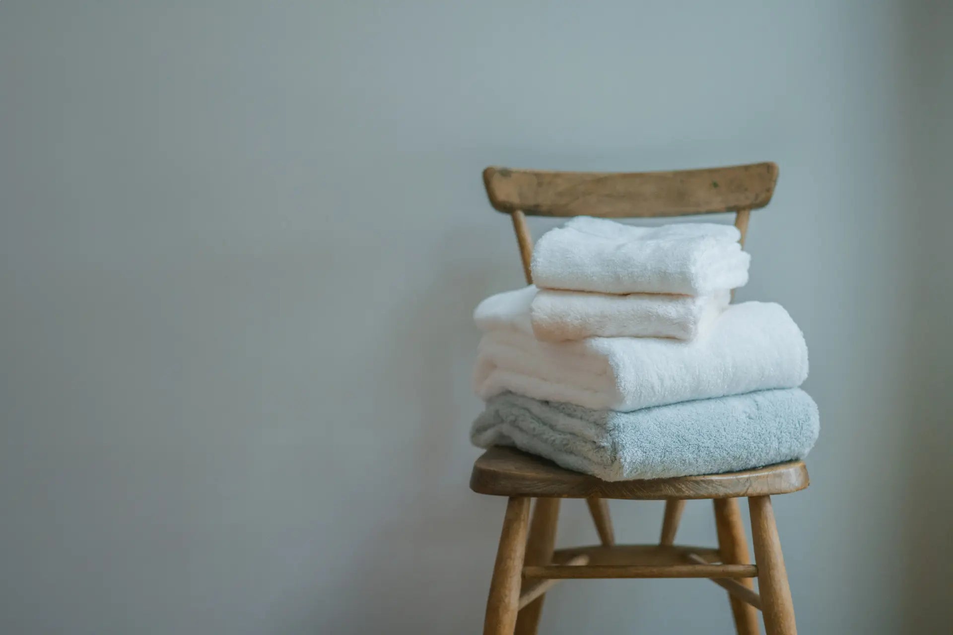 Stack of luxury Imabari towels on a wooden chair against a plain background