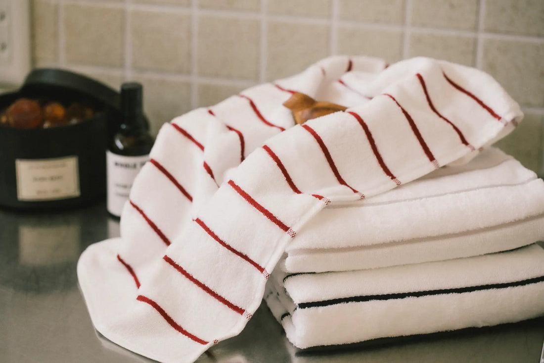 A stack of folded white Imabari  towels with red, gray and navy  stripes on the bath room