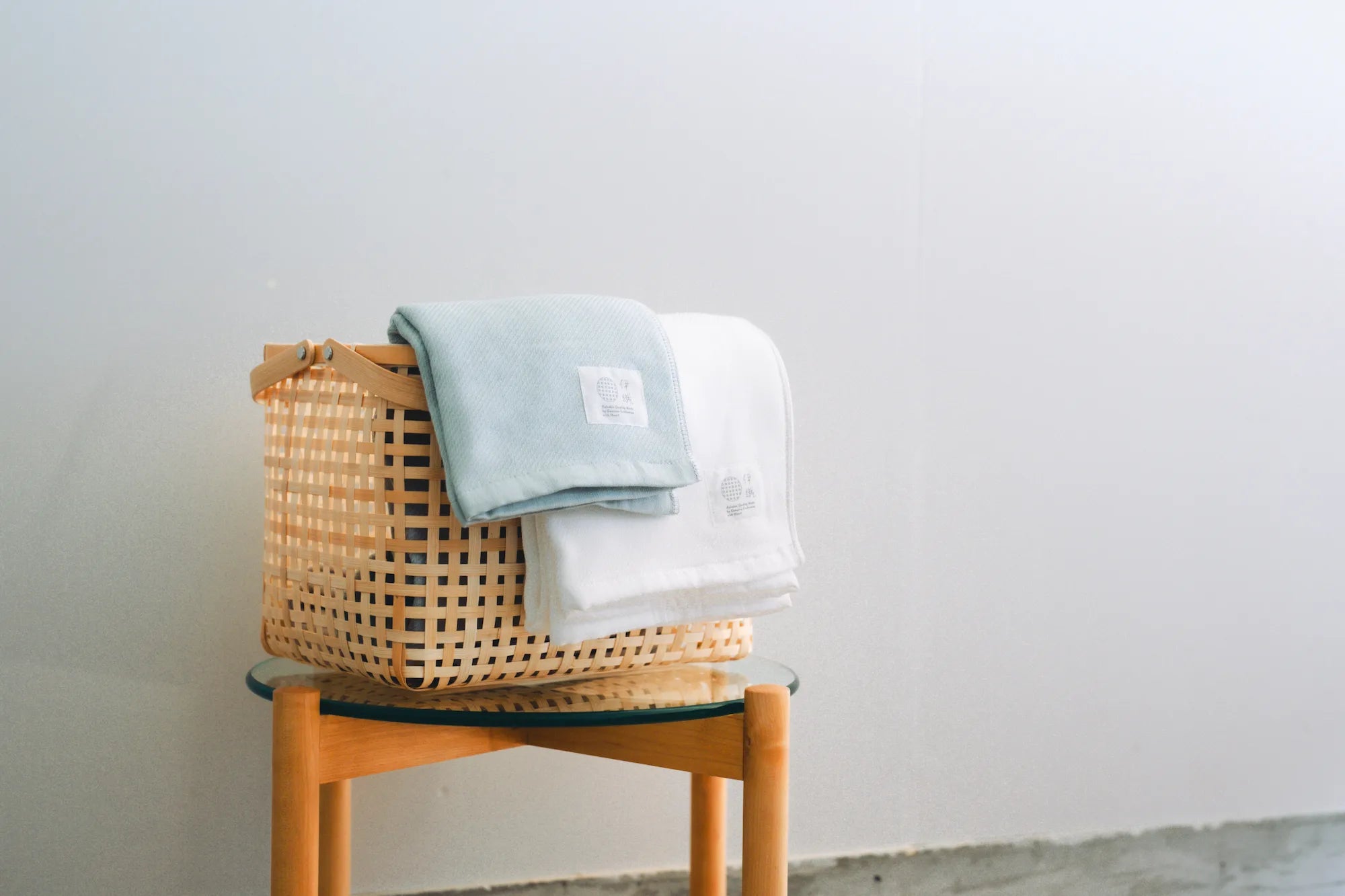 Folded Imabari towels in white and blue colors made from cotton gauze in the basket, branded with a label showing the name &