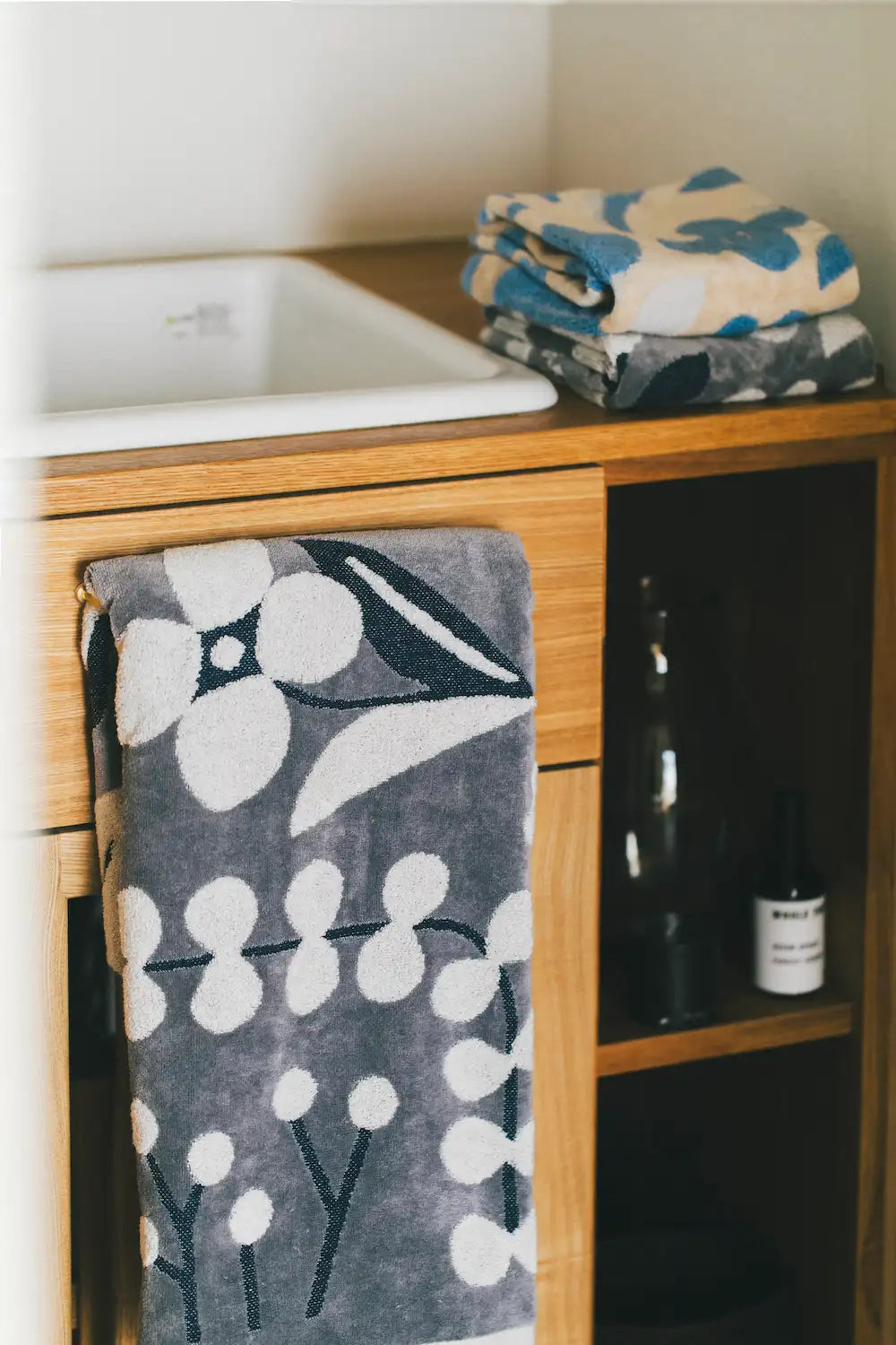 Hang a gray Imabari towel with floral pattern and stack of gray and beige folded Imabari towel in the bath room